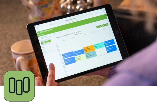 Ein Tablet zeigt einen Terminkalender aus JCC-Personalplanung. Links unten ist das grüne Icon dieser Anwendung zu sehen.