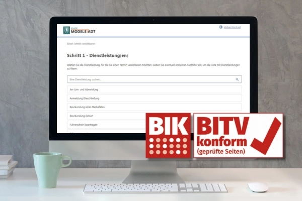 Ein Monitor auf einem Schreibtisch. Auf dem Bildschirm ist das Online-Terminportal einer Stadt Modellstadt zu sehen. Im Vordergrund befindet sich das Logo des BIK "BITV konform (geprüft)".