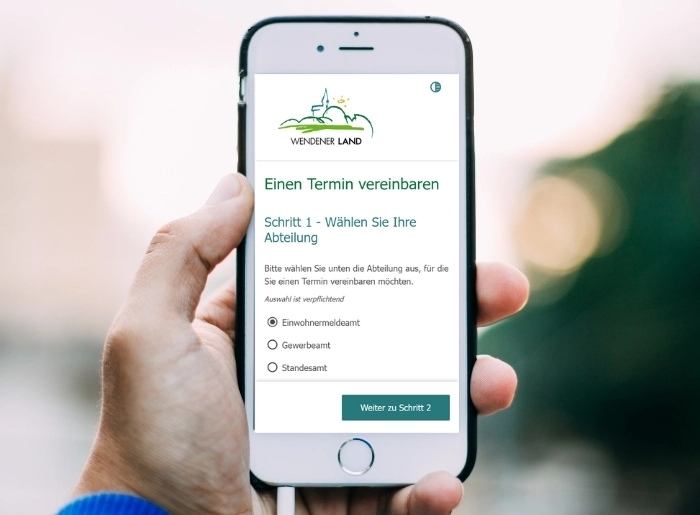 Eine Person hält ein Smartphone in der Hand, auf diesen man das Online-Terminportal der Gemeinde Wenden sieht.